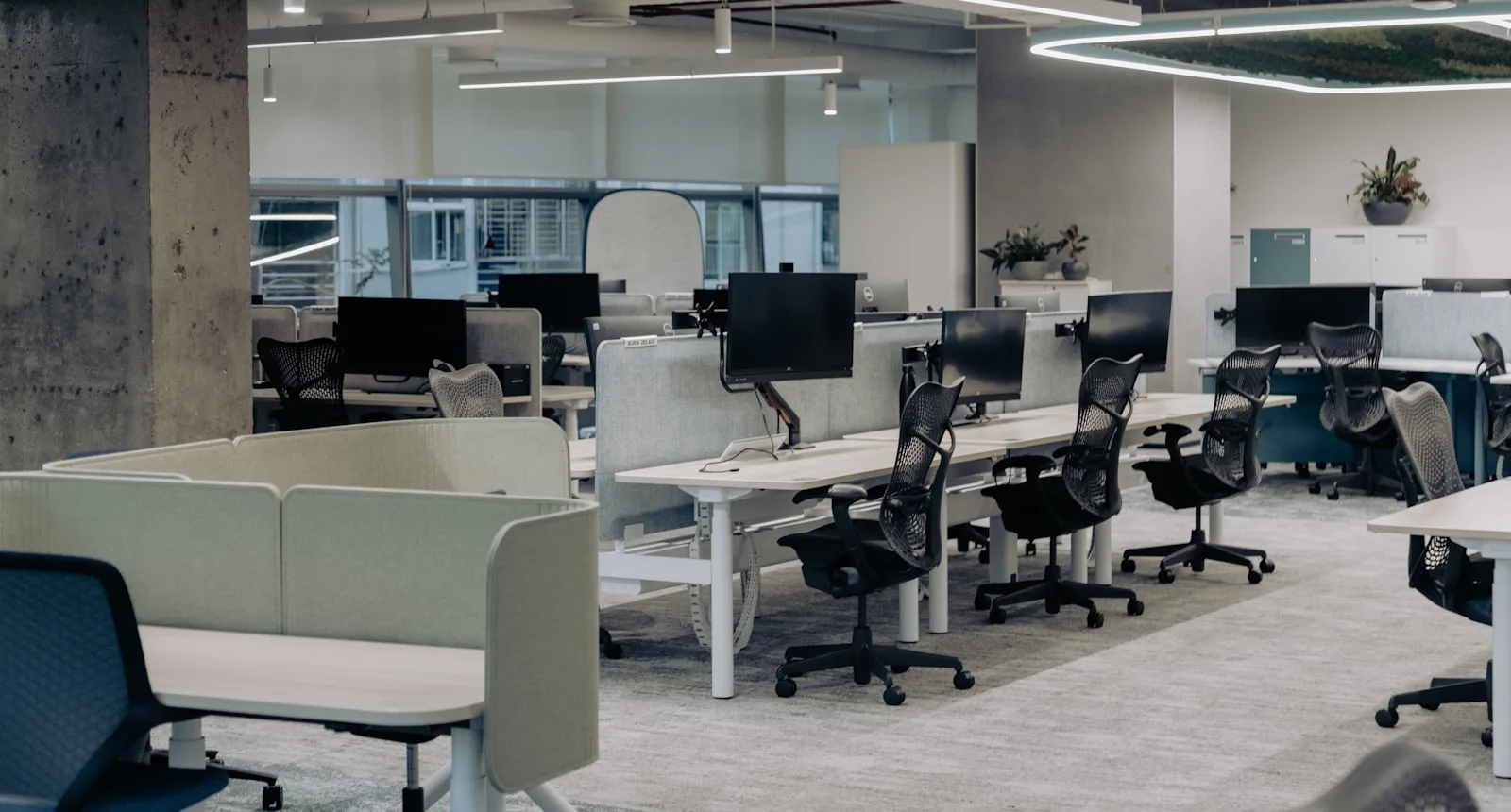 An empty open-plan office with rows of desks and monitors, chairs pushed in, no one at their seats.